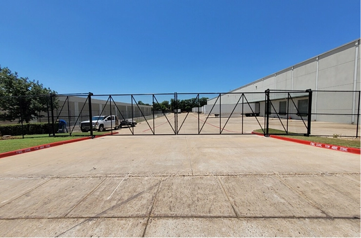 A wide black chain-link cantilever slide gate with a heavy-duty steel frame securing a large commercial loading dock area.