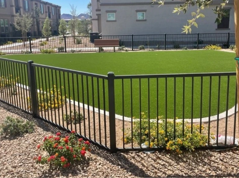 A black aluminum ornamental fence with vertical pickets and square posts enclosing a green lawn area in a commercial or public space.